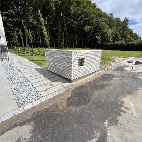 Murstens-tilbygning i hvid mursten ved indkørsel og have.