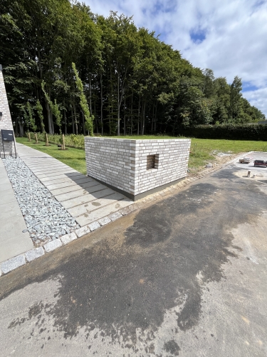 Murstens-tilbygning i hvid mursten ved indkørsel og have.